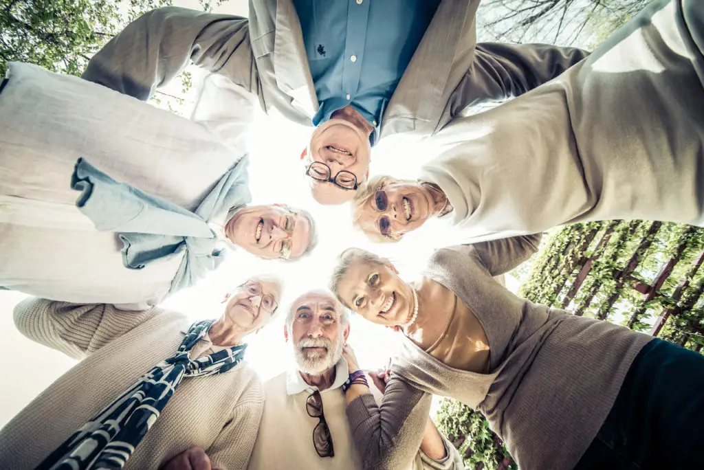 Séniors en rond qui sourient en se tenant les bras